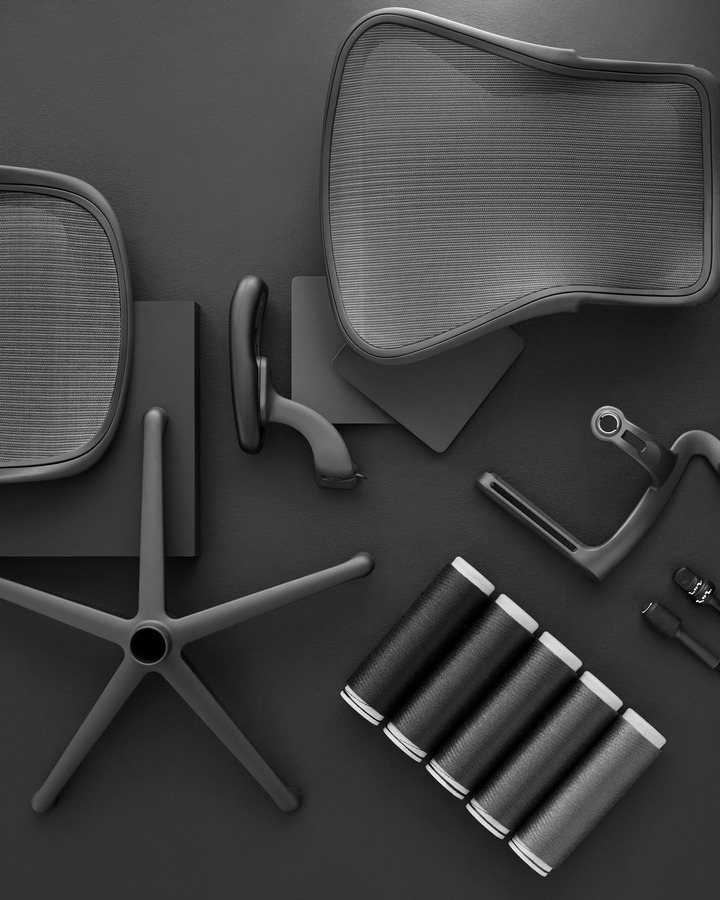 Een verzameling Herman Miller stoelcomponenten gerangschikt op een donker oppervlak. Inclusief mesh rugleuningen, een zittingbasis, armleuningen en een rollende basis met vijf spaken, die allemaal moderne ergonomische designelementen laten zien, wat de bekwame samenwerking van ontwerpers benadrukt.