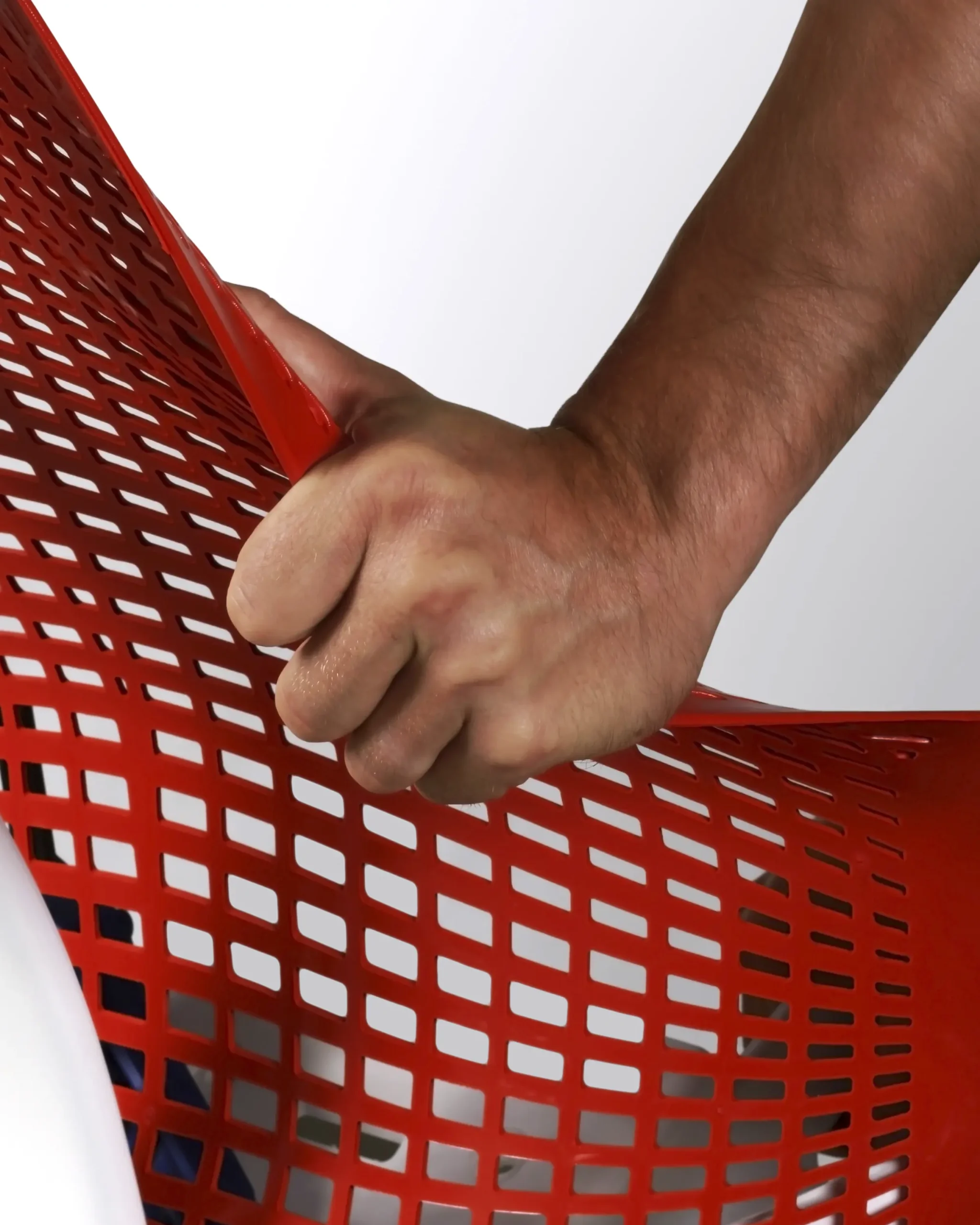 Een hand grijpt een flexibel rood plastic gaas vast, wat de rekbaarheid ervan demonstreert met precisie die vergelijkbaar is met het ontwerp van Herman Miller. De achtergrond is een effen, lichtgrijze kleur.